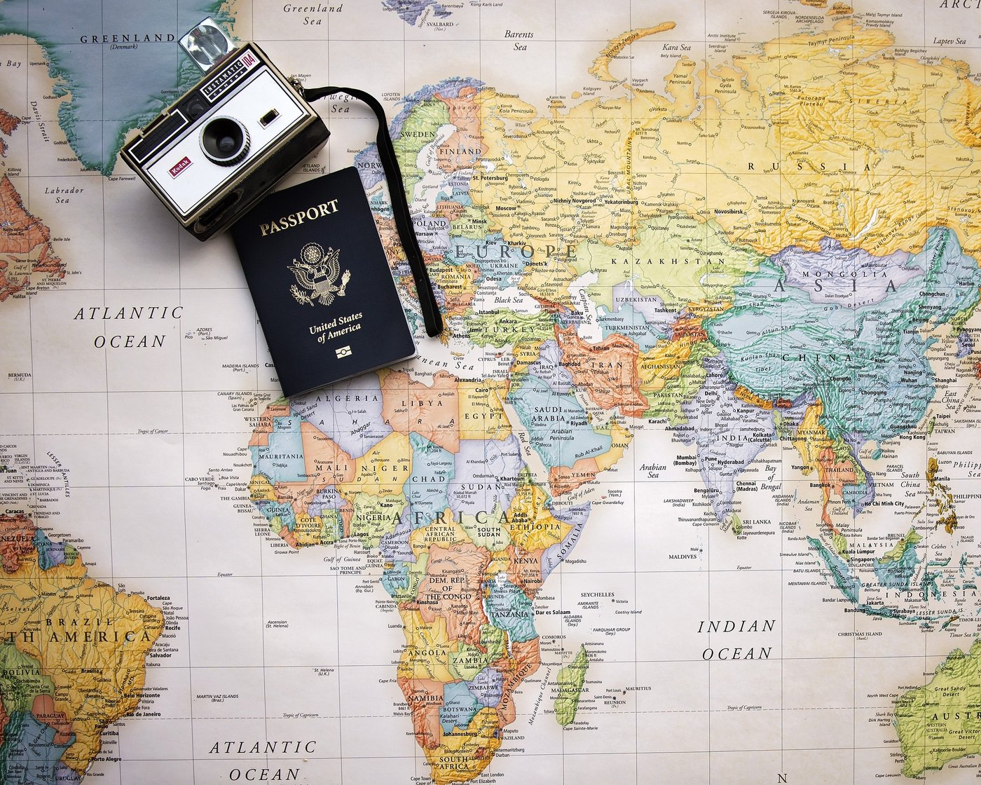 Das Bild zeigt eine Weltkarte mit einem Pass und einer Kamera